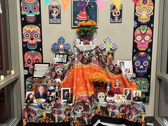 Brightly colored Dia de los Muertos altar with colorful skull design and many photographs on the table. 