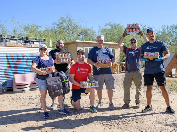 Six faculty and Doctor of Nursing Practice residents stand together outside holding cases of food and supplies to donate. 