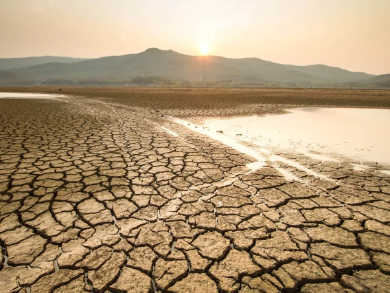 receeding lake with dried cracked ground in the foreground and mountain in background