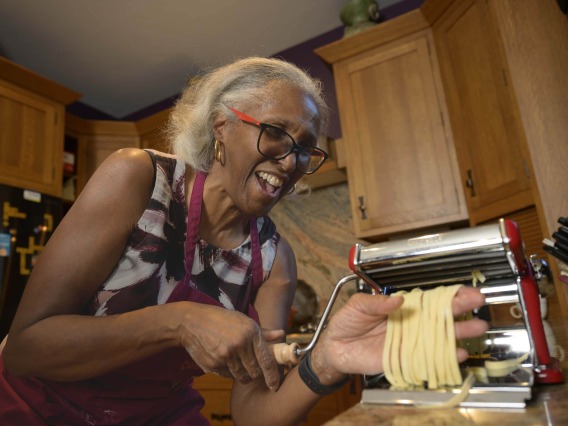 Woman making fresh pasta in her kitchen while smiling joyfully.
