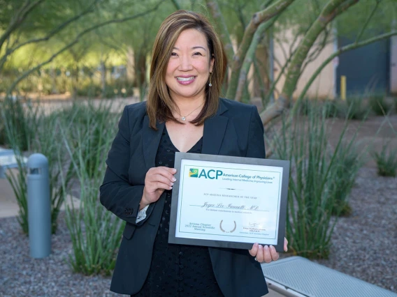 Dr. Joyce Lee-Iannotti standing outside smiling holding a certificate. She is an Asian woman with medium length strait brown hair with highlights. 