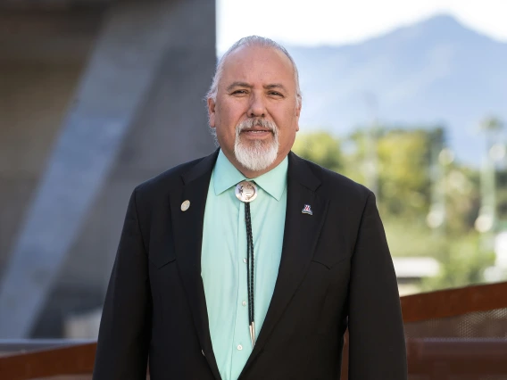 Dr. Carlos Gonzales standing outside in a suit coat and bolo tie. 