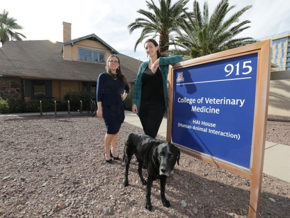 Two women standing next to College of Veterinary Sciences sign with dog.