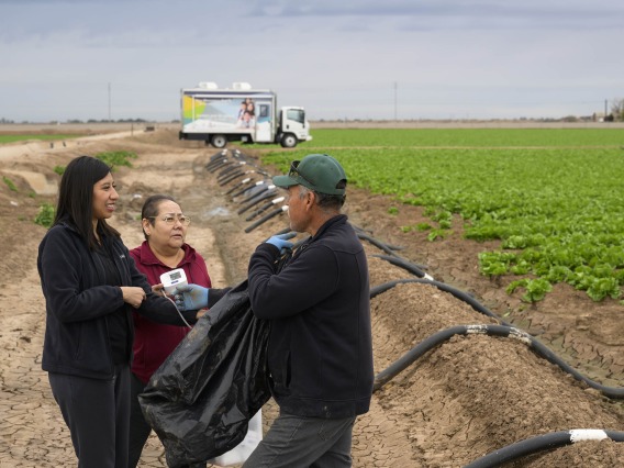 Sheila Soto and health educator Andrea Contreras, speak to a man in the middle of a farm field in San Luis, Arizona.