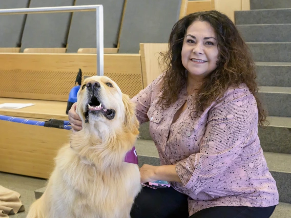 A woman sits on some stairs while petting a golden retriever, who almost looks to be smiling. 