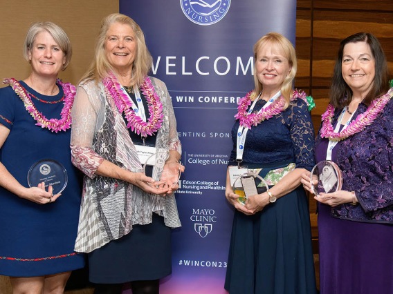 Four female professors from the University of Arizona College of Nursing stand next to each other smiling and holding awards.