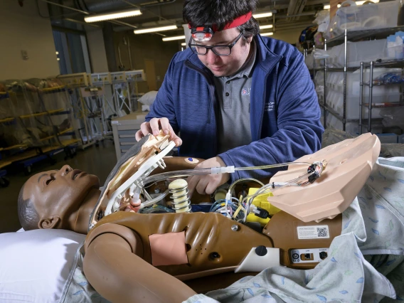 Lucas Grijalva reaches inside a simulation manikin to check on its interior parts. 