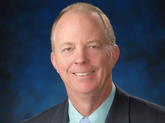 Portrait of a middle-aged balding white man wearing a suit coat and smiling.
