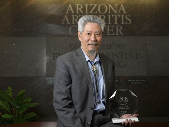 Portrait of a man standing in a suit in front of the Arizona Arthritis Center sign. 