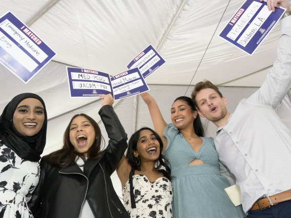 Five College of Medicine – Tucson fourth-year medical students hold up small signs in celebration after finding out where they matched for residency. 