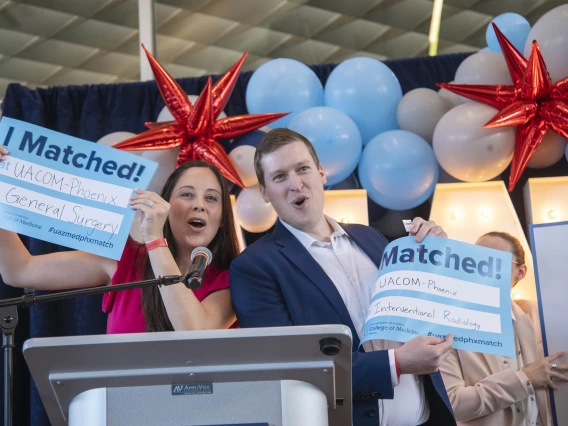 Two fourth-year medical students from the University of Arizona College of Medicine – Phoenix stand at a podium holding up signs that say “I Matched!” as they announce where they are headed for residency. 