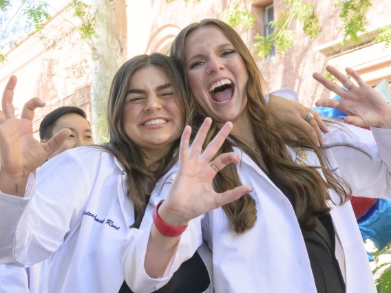 Two University of Arizona R. Ken Coit College of Pharmacy students smile and make the Wildcat sign with their fingers as they walk outside after receiving their white coats.