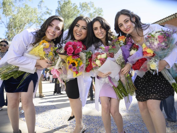 Four University of Arizona R. Ken Coit College of Pharmacy students, all holding flowers and smiling, stand together. 