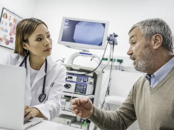 doctor with laptop talks to patient in hospital room