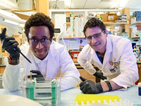 A student and professor, both wearing white lab coats, pose for a photo in a laboratory