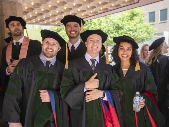 Five University of Arizona College of Medicine – Phoenix students dressed in graduation regalia stand together smiling before their commencement ceremony.