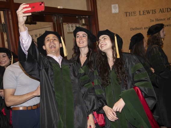 Three University of Arizona College of Medicine – Phoenix students dressed in graduation regalia take a selfie. 