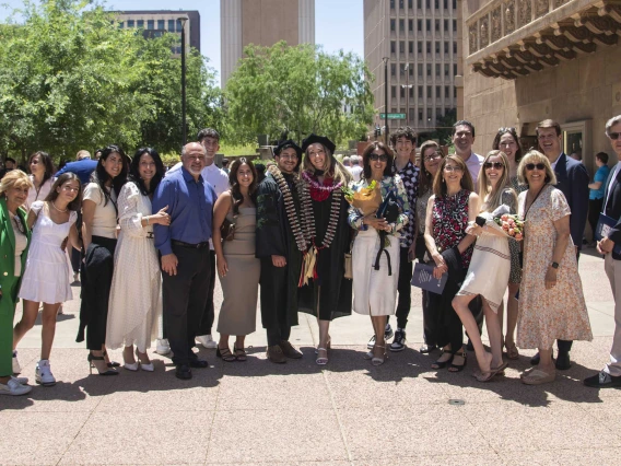 A large group of family members stand on each side of two University of Arizona College of Medicine – Phoenix graduates wearing their caps and gowns. 