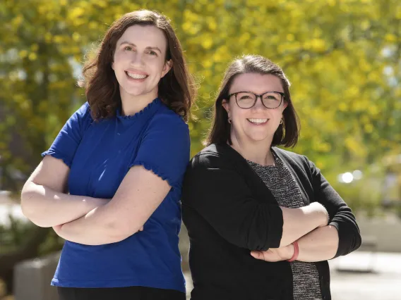 Portrait of Leslie Farland and Jessica Rainbow outside standing back to back. 