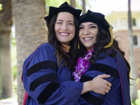 Two University of Arizona College of Nursing graduates in caps and gowns smile as they hug. 