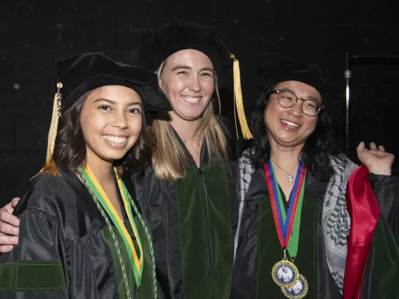 Three University of Arizona College of Medicine – Tucson students in graduation caps and gowns stand together, smiling.  