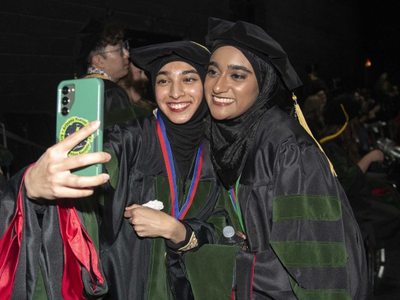 Two University of Arizona College of Medicine – Tucson students in graduation regalia take a selfie before their graduation ceremony.