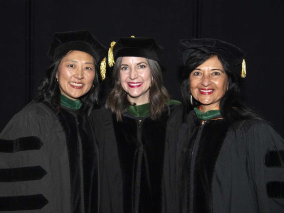 Three University of Arizona College of Medicine – Tucson professors in graduation caps and gowns stand together, smiling.  