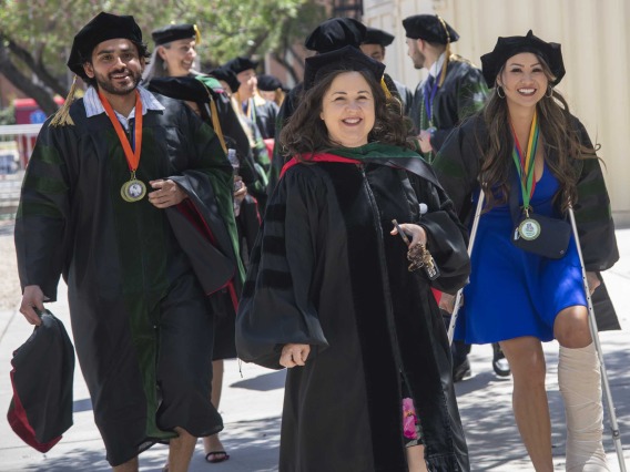 Faculty and students from the University of Arizona College of Medicine – Tucson, dressed in graduation caps and gowns, walk outside on their way to the commencement ceremony. 