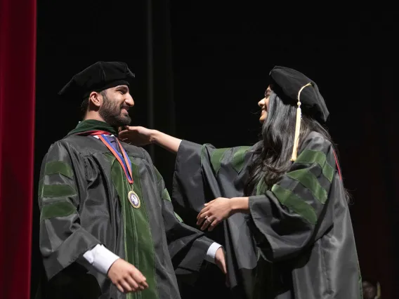 Two people dressed in caps and gowns reach for each other to hug during the University of Arizona College of Medicine – Tucson graduation ceremony. 