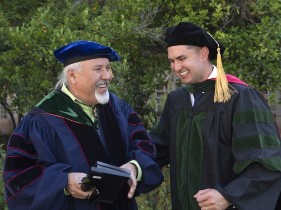 A University of Arizona College of Medicine – Tucson professor laughs with a recently graduated medical student after the commencement ceremony. Both are dressed in graduation caps and gowns. 