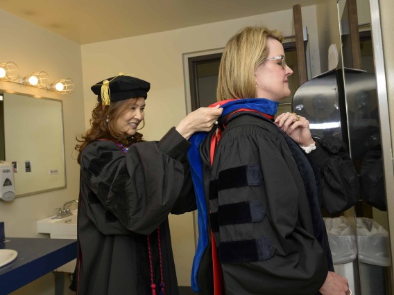 A University of Arizona R. Ken Coit College of Pharmacy faculty member dressed in graduation regalia helps another faculty member straighten her hood. 