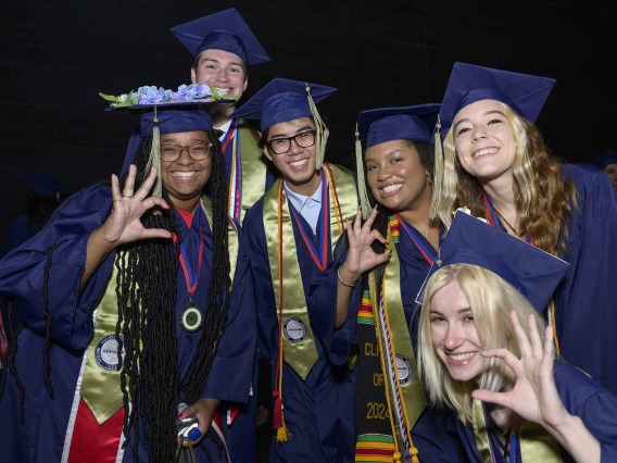 Six University of Arizona R. Ken Coit College of Pharmacy students dressed in graduation caps and gowns show the “Wildcat” hand sign while smiling. 