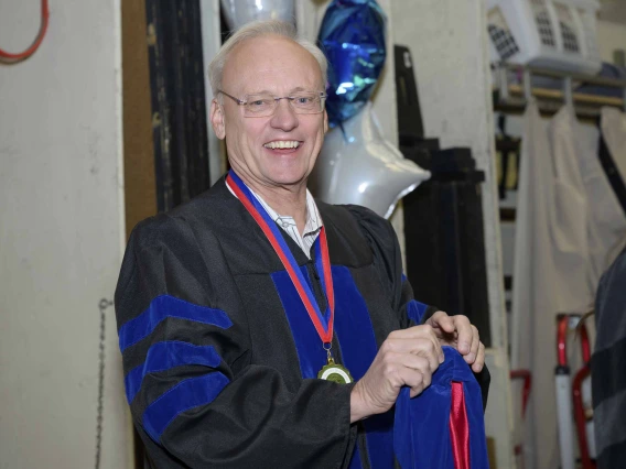 Rick Schnellmann, dean of the University of Arizona R. Ken Coit College of Pharmacy, smiles as he puts on his cap and gown. 