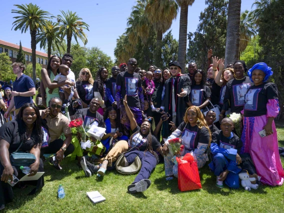 About 20 friends and family members surround a University of Arizona R. Ken Coit College of Pharmacy graduate who stands in the middle of the group wearing his graduation cap and gown. 