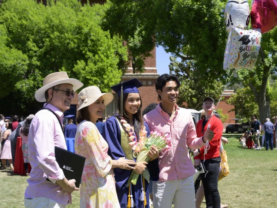 A University of Arizona R. Ken Coit College of Pharmacy graduate wearing a cap and gown holds flowers while standing with her parents and brother. 