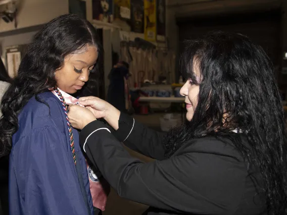 A University of Arizona Mel and Enid Zuckerman College of Public Health student wearing a graduation gown has a pin put on her gown by a staff member.  