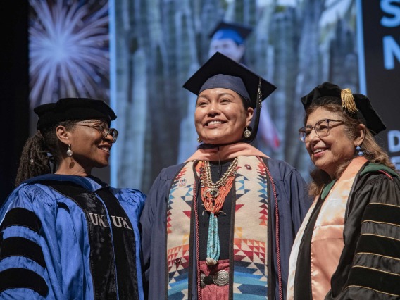 A University of Arizona Mel and Enid Zuckerman College of Public Health student smiles as she stands between two faculty members. All are wearing graduation regalia.