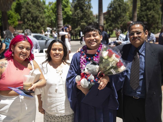 A University of Arizona Mel and Enid Zuckerman College of Public Health student smiles while holding flowers, flanked by three family members. The student is wearing a graduation gown. 