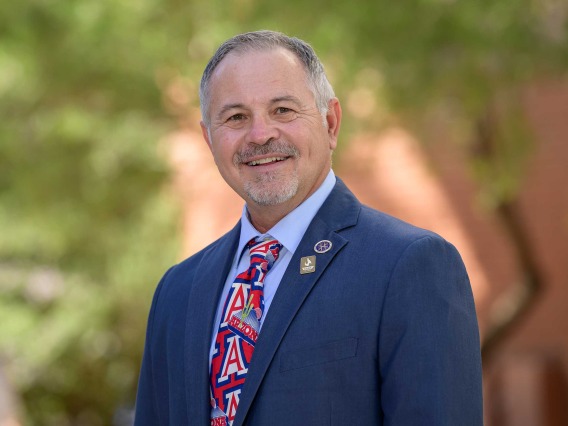 A portrait of UArizona College of Nursing professor Jim Reed wearing a suit and tie and smiling in an outdoor setting