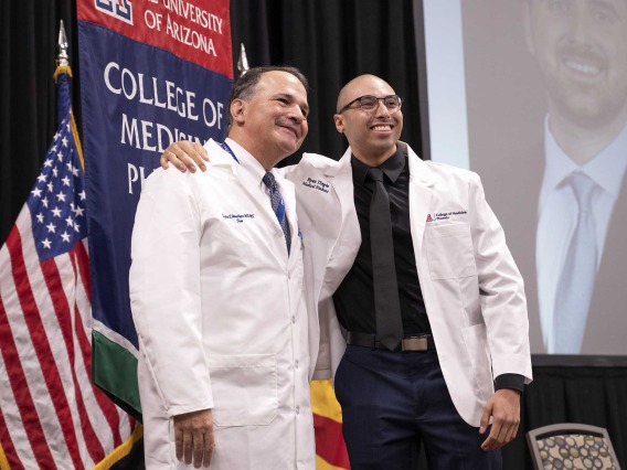 University of Arizona College of Medicine – Phoenix Dean Fred Wondisford poses for a photo with a new medical student. Both are wearing white medical coats.