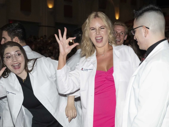 Several incoming University of Arizona College of Medicine – Tucson students wearing medical white coats wave, smile and flash the Arizona Wildcats hand sign. 