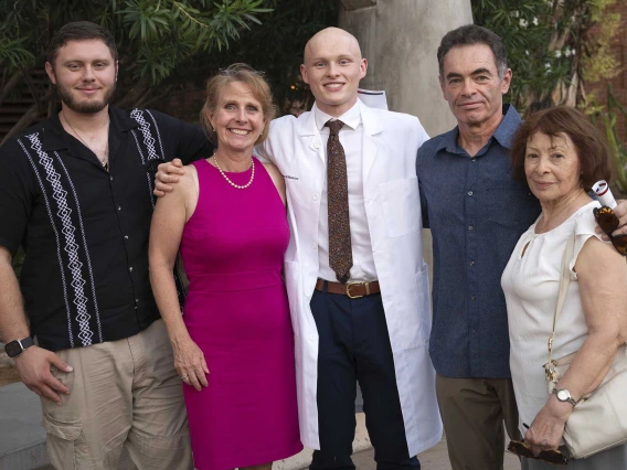 An incoming University of Arizona College of Medicine – Tucson student wearing a medical white coat stands with several family members outdoors. 