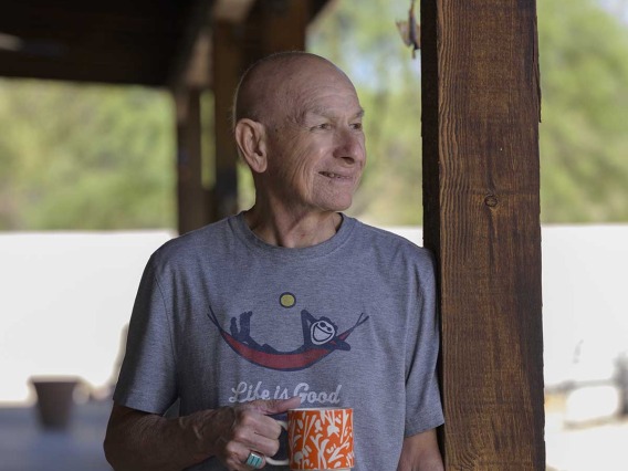 cancer survivor holding a coffee mug, standing on a patio and looking toward backyard