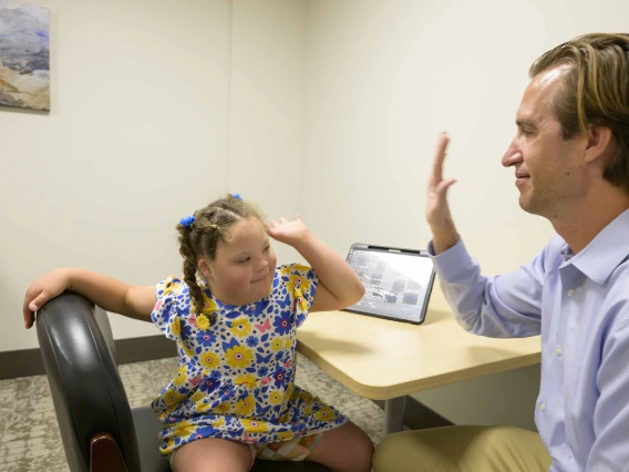 Dan Combs, MD, assistant professor in pediatrics and sleep medicine at the University of Arizona College of Medicine – Tucson’s Department of Medicine, holds his hand up to a young Down syndrome patient for a high five in an office.