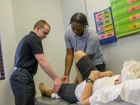 A physical therapist provides instruction to a student observing how to work with clients in a clinic.