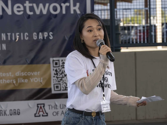 A woman in a white shirt speaks into a microphone. 