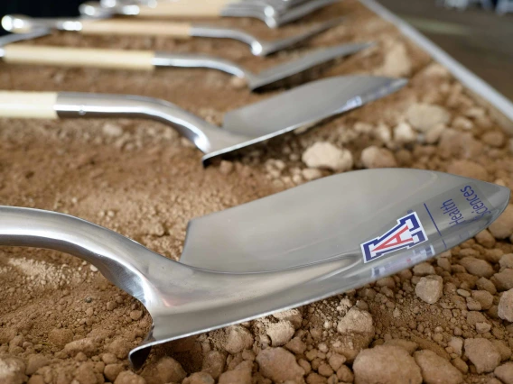 Several silver shovels with the University of Arizona logo on them lay in the dirt. 