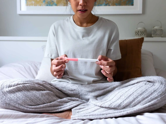 A young woman reads a pregnancy test as she sits up in bed wearing pajamas.