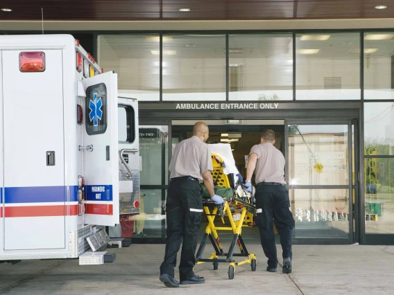 Paramedics move a patient on a stretcher from an ambulance into a hospital.