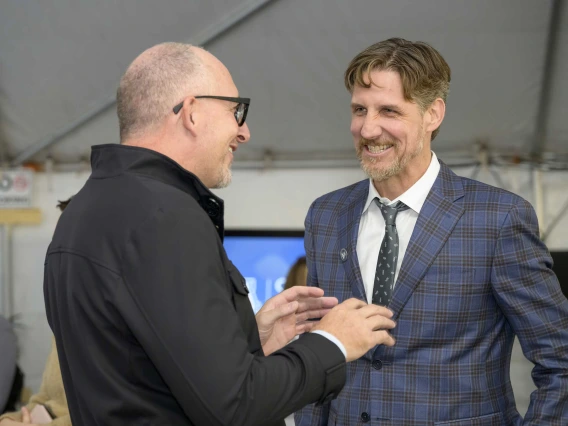 Two smiling men in dark coats face each other as they talk.